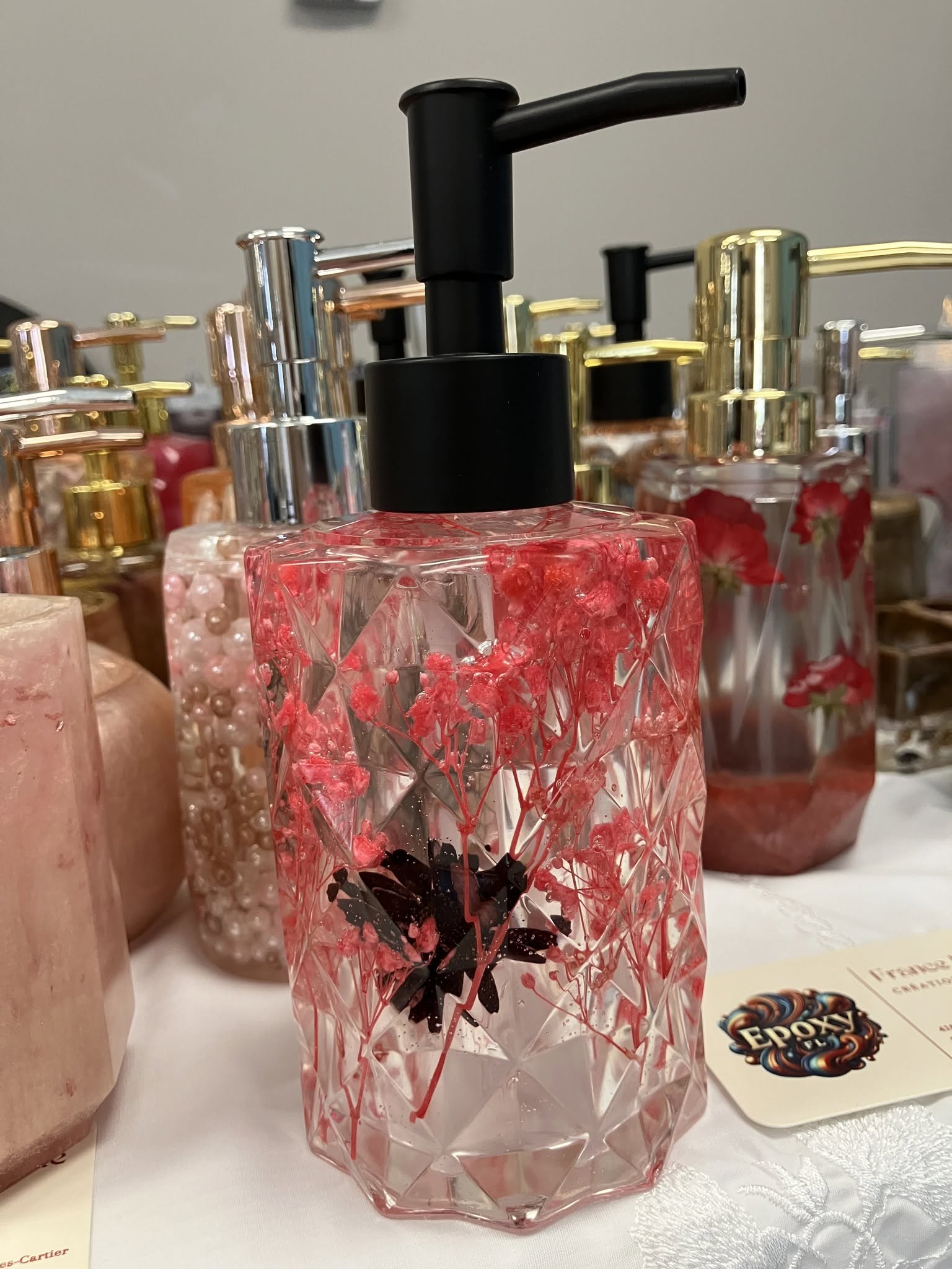 Distributeur à savon transparent en résine époxy avec fleurs rouges et pompe noire.
